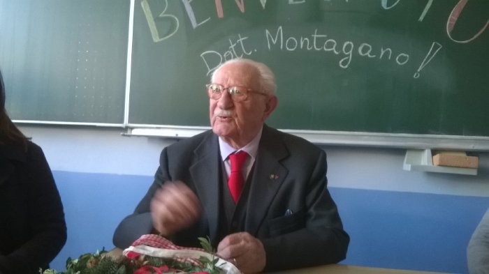 Michele Montagano sitzend vor einer Tafel auf der Bienvenuto Dott. Montagano in bunten Buchstaben geschrieben steht.